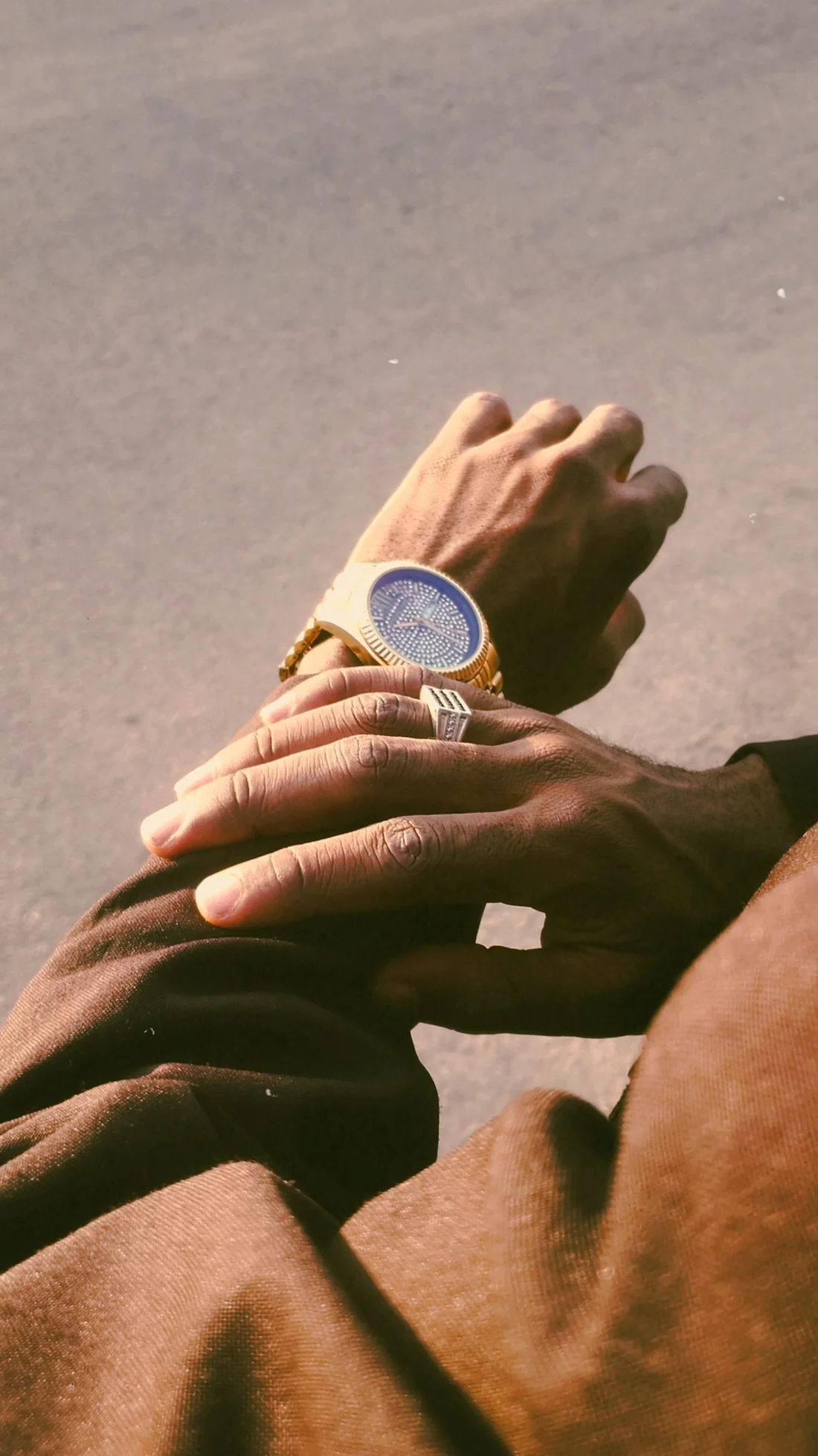 Man's hands wearing a gold ring and gold watch in warm sunlight
