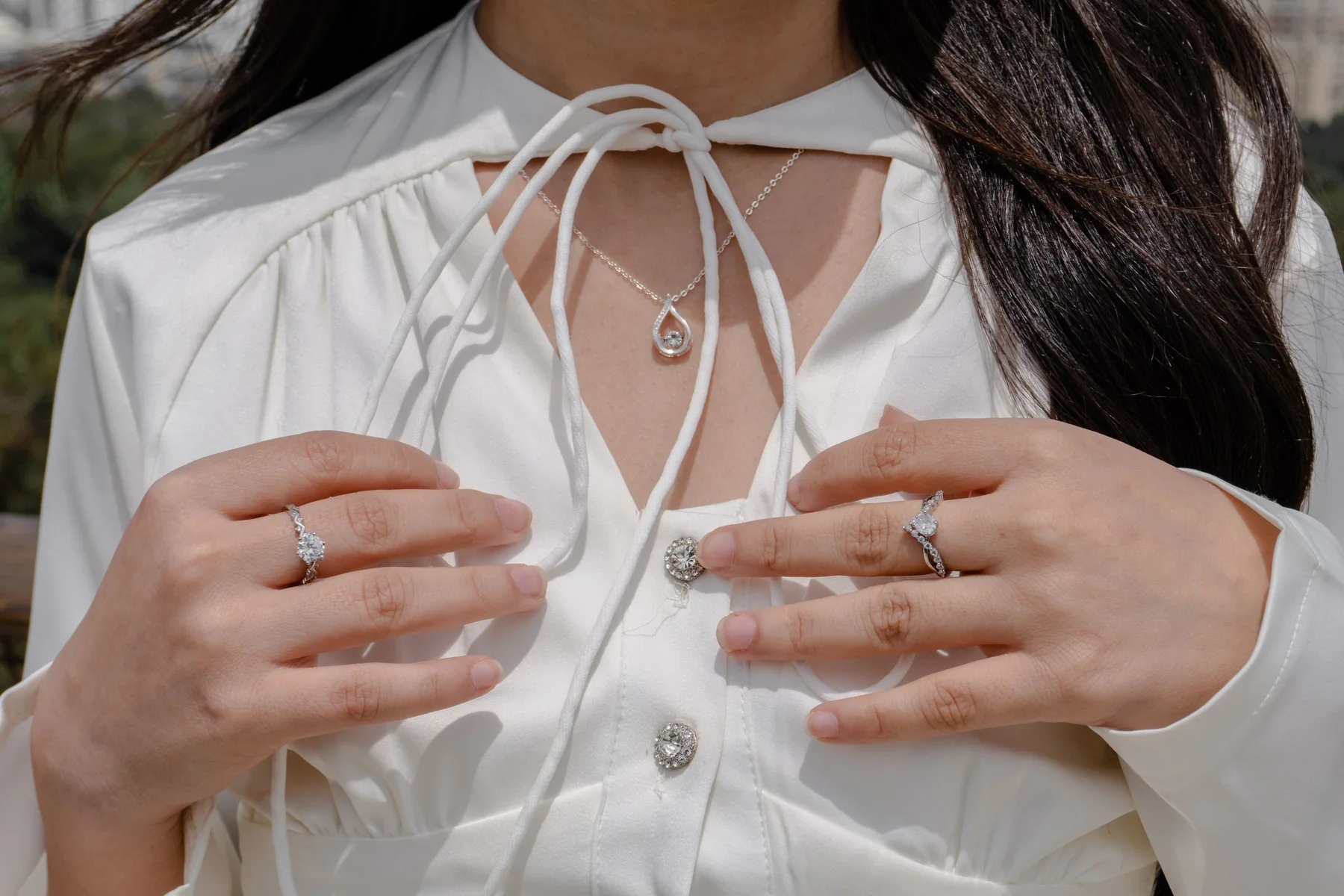 Woman in a white blouse wearing diamond rings and a teardrop diamond necklace