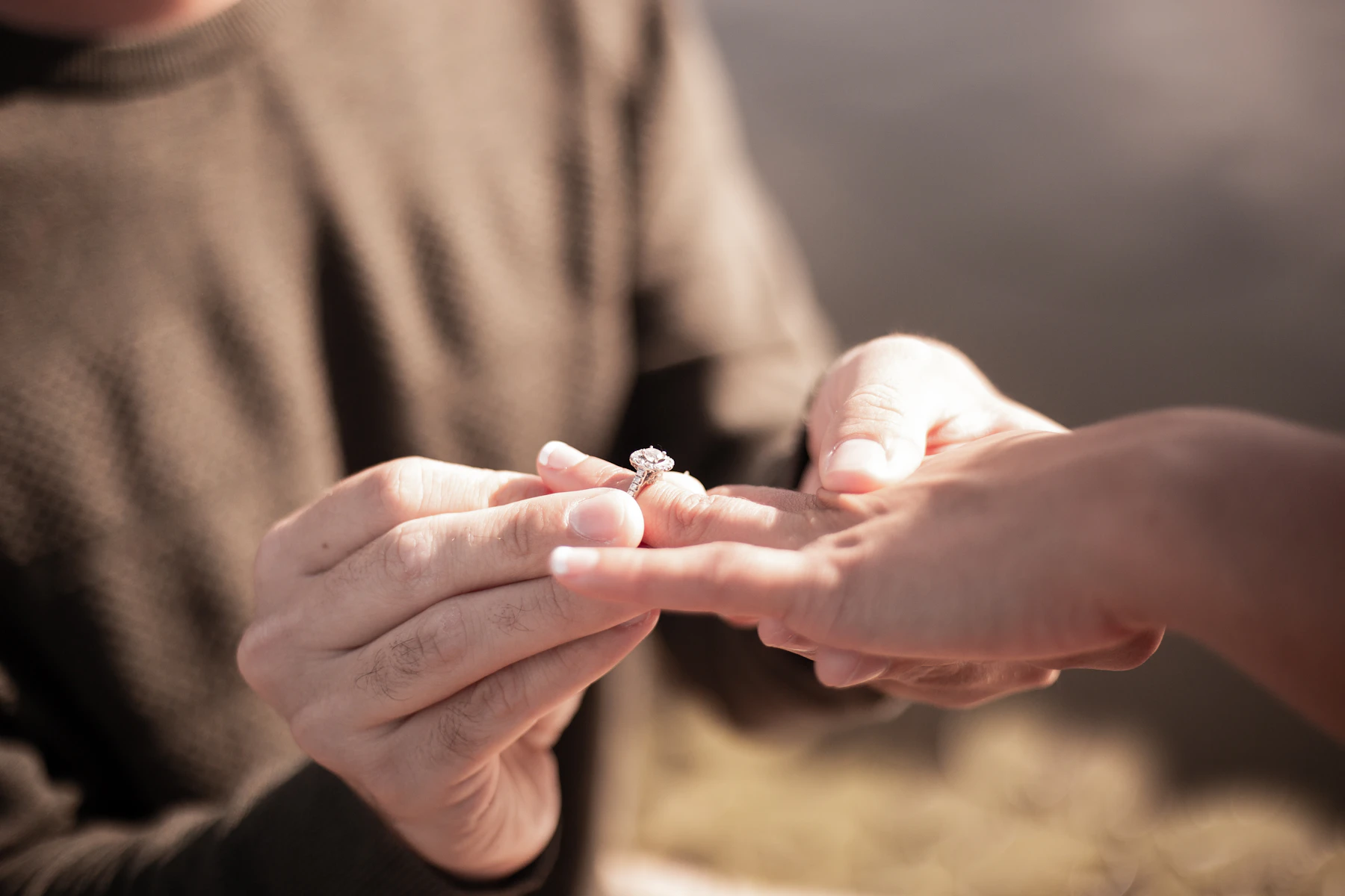 A diamond engagement ring being placed on a hand