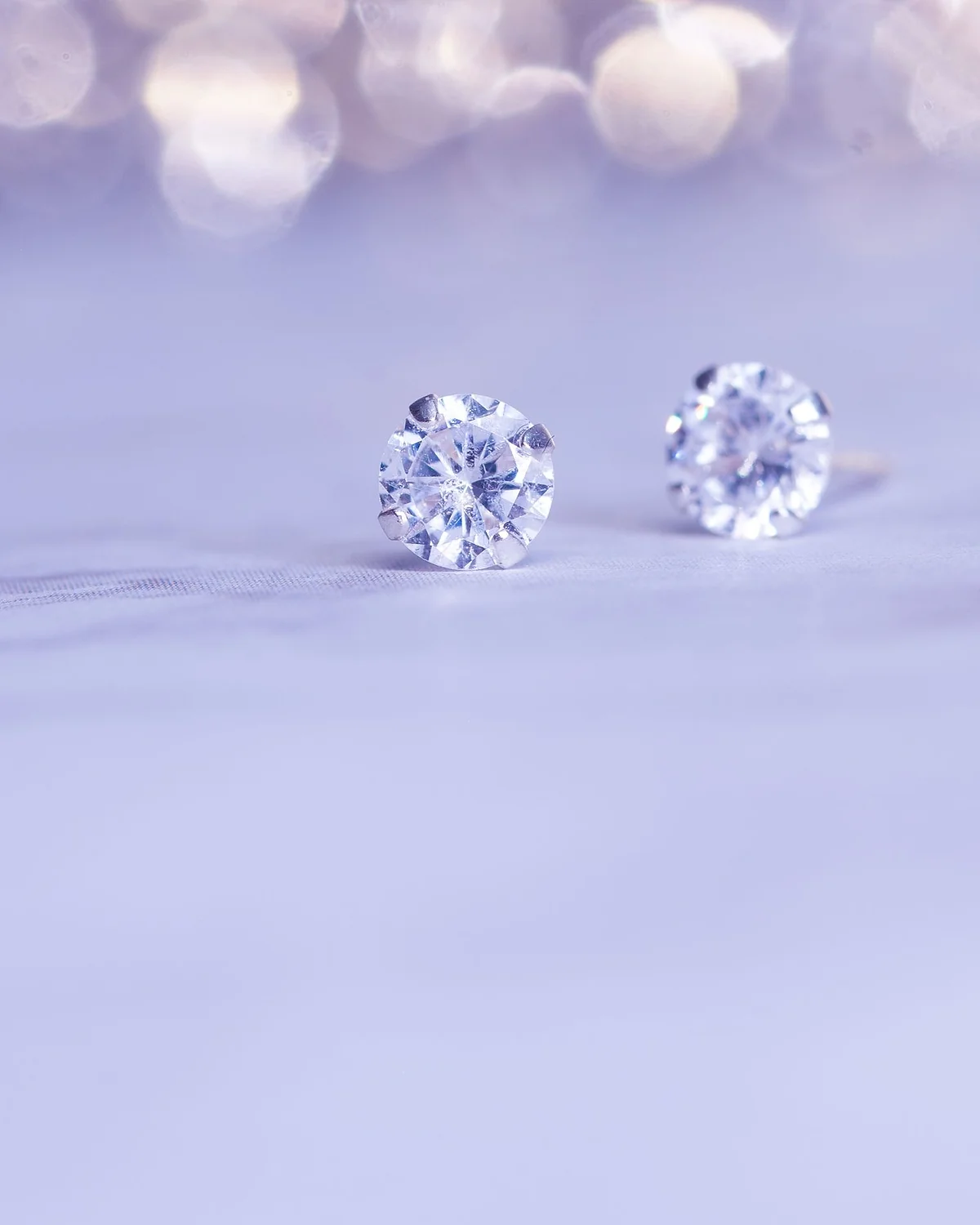 Pair of round diamond stud earrings on a soft lavender surface