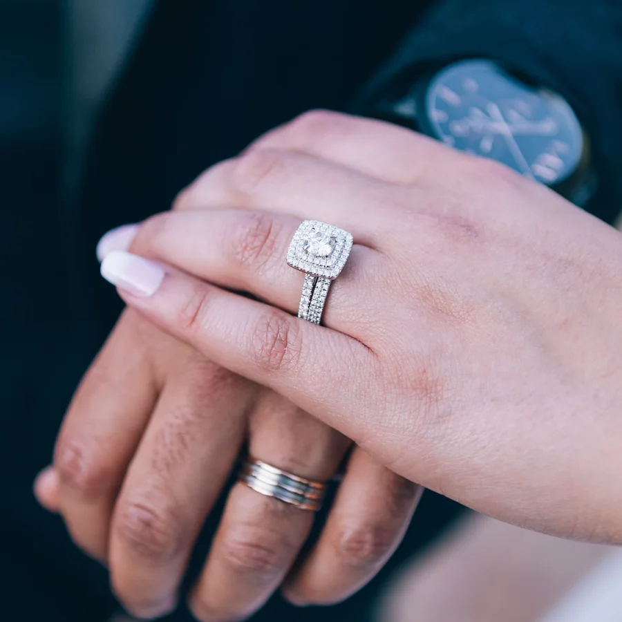 A finished double halo diamond engagement ring worn on a hand