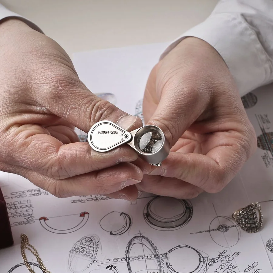 A jeweler checking a ring through a loupe over design drawings