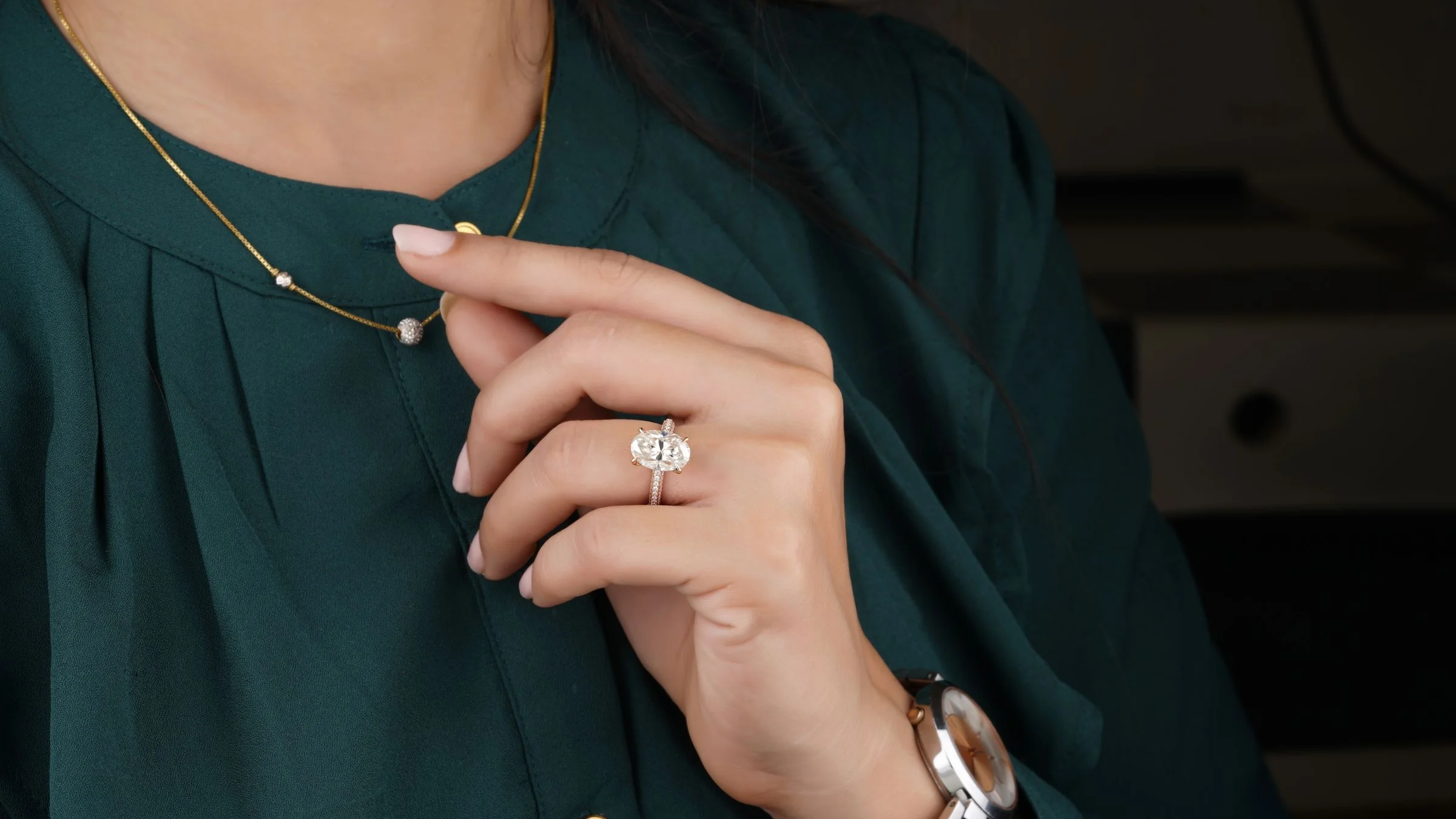 A woman in a green blouse wearing an oval diamond engagement ring and a fine gold necklace