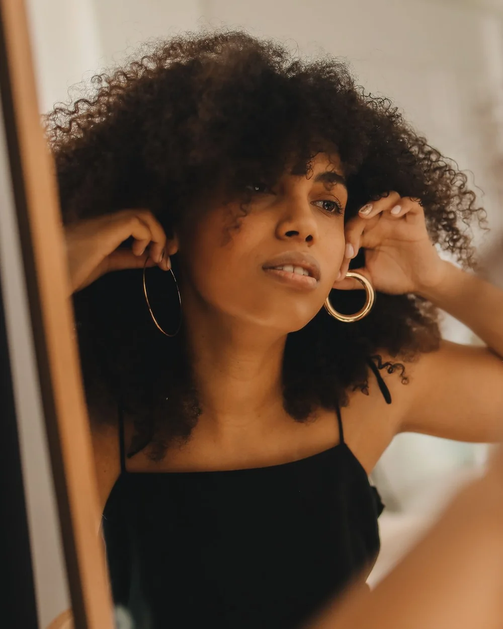 A woman trying on gold hoop earrings in a mirror