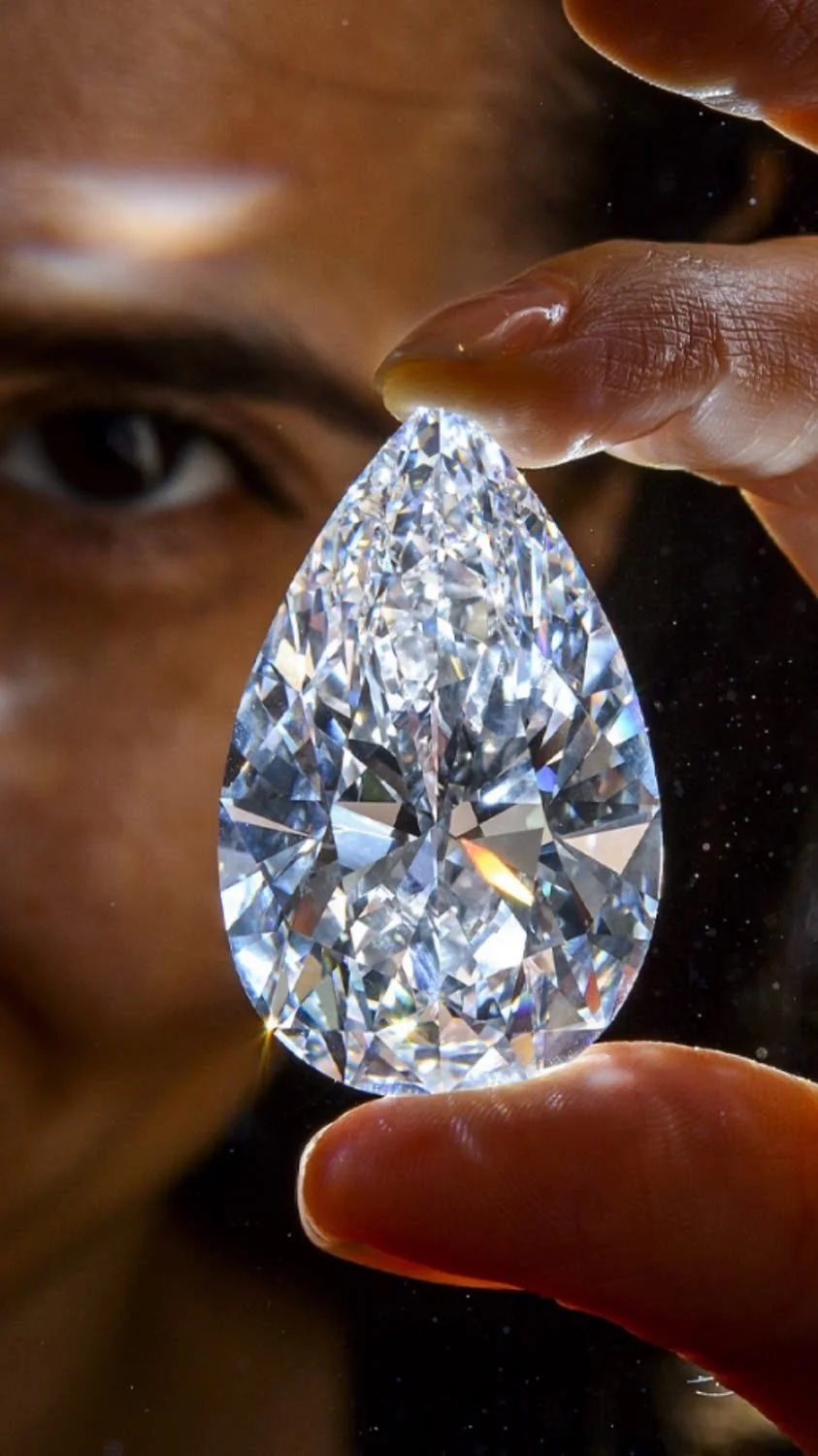 A flawless pear-shaped diamond held up to the light between two fingertips